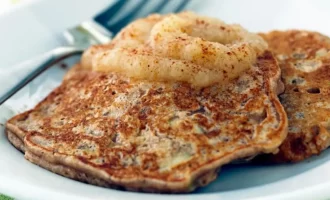 Two golden-brown pancakes topped with a dollop of applesauce and a light sprinkle of cinnamon sit on a plate.