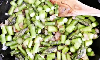 Chopped asparagus and onions are sautéed in a black skillet with a wooden spoon, creating a fresh and earthy tone.