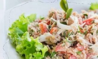 A fresh tuna salad with vibrant lettuce, shredded tuna, and diced tomatoes, garnished with herbs.