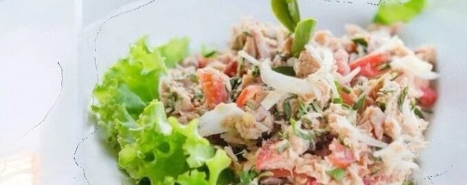 A fresh tuna salad with vibrant lettuce, shredded tuna, and diced tomatoes, garnished with herbs.