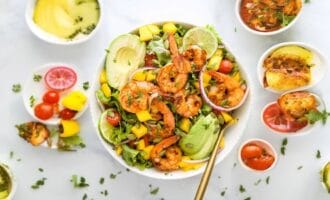 A colorful shrimp salad with avocado, lime, mango, and greens in a bowl.