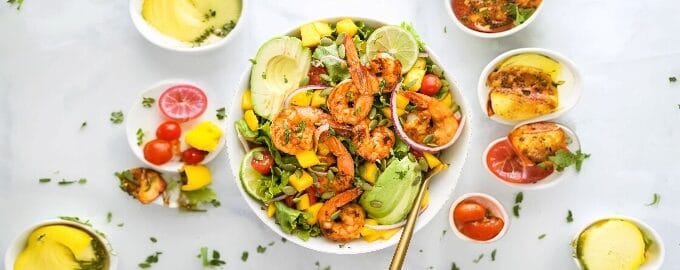 A colorful shrimp salad with avocado, lime, mango, and greens in a bowl.