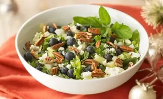 A vibrant salad in a white bowl featuring blueberries, pecans, feta cheese, and fresh greens.