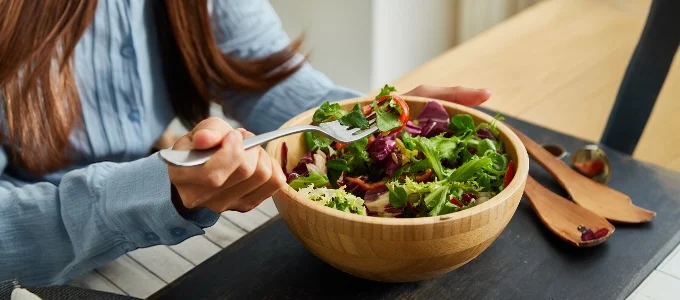A person in a blue shirt holds a fork with salad over a wooden bowl
