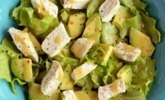 A fresh salad in a blue bowl features crisp lettuce, diced chicken, and avocado.