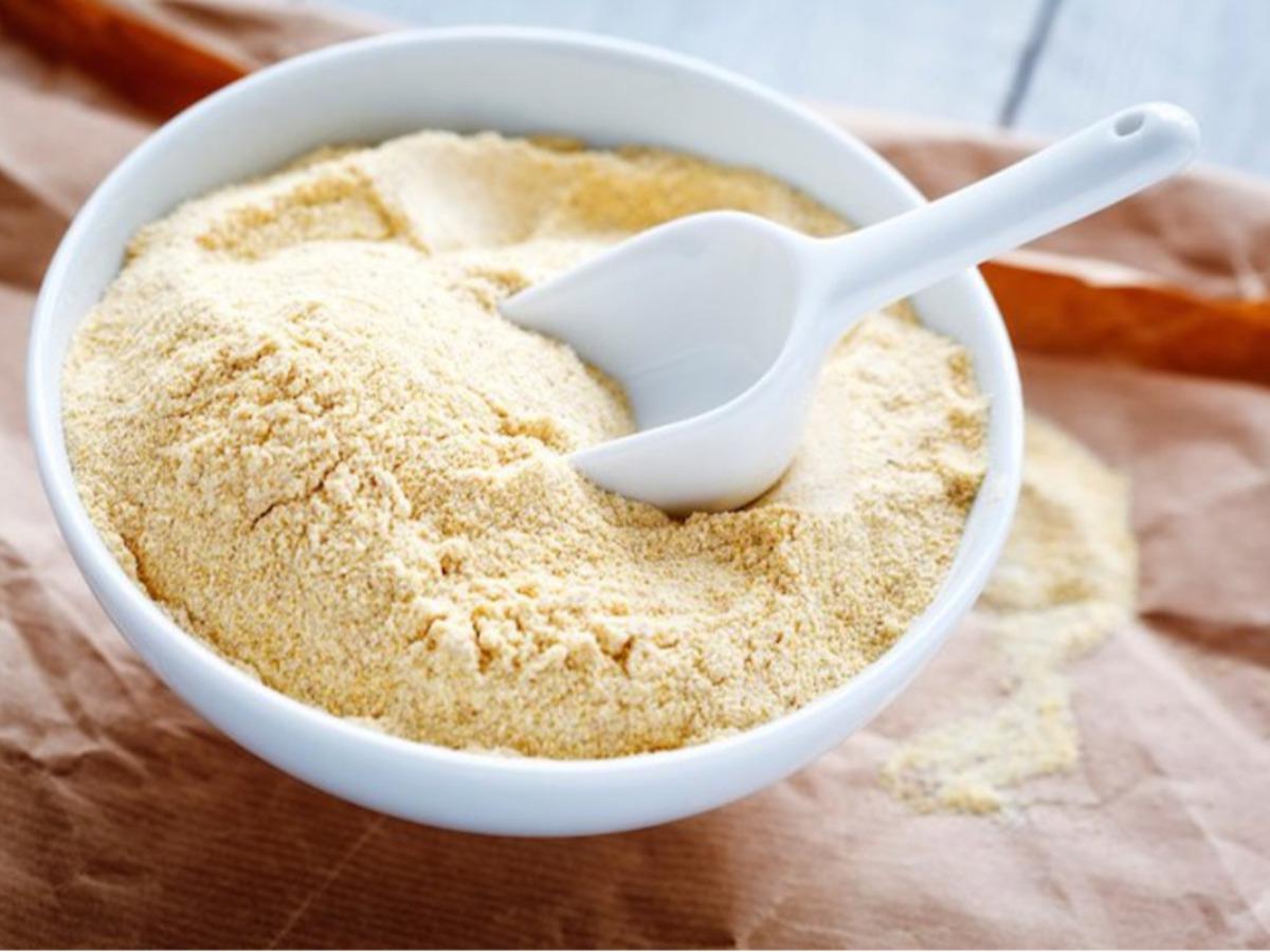 A white bowl filled with yellow cornmeal, accompanied by a small white scoop, rests on Chickpea flour.