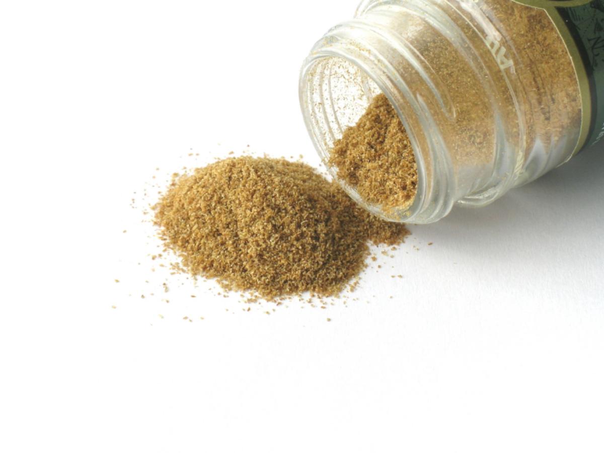 Cumin, spilling fine brown cumin powder onto a white surface.