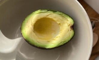 A ripe half avocado with a smooth pit rests in a white bowl