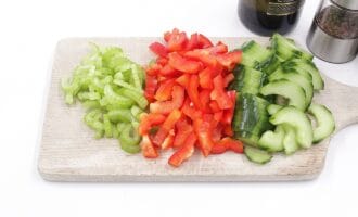 Chopped celery, red bell peppers, and cucumbers on a wooden cutting board.