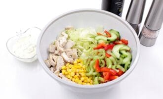 A white bowl filled with chopped chicken, lettuce, cucumber, corn, red bell pepper, and celery.