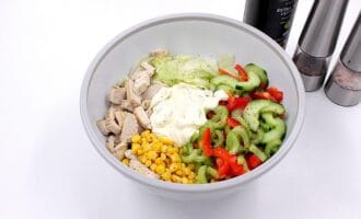 A fresh salad in a white bowl with diced chicken, lettuce, sliced cucumbers, red peppers, celery, corn