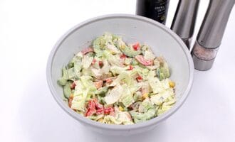 A mixed salad in a white bowl with lettuce, tomatoes, cucumber, and corn, on a white surface.