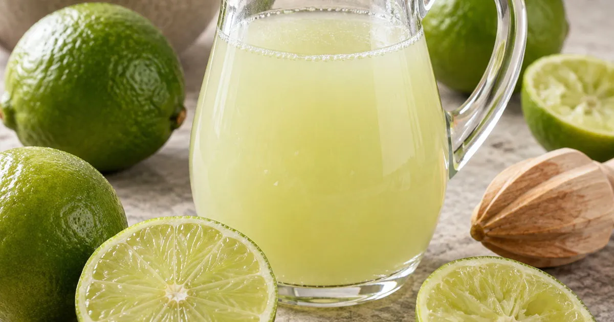 Fresh lime juice in a glass pitcher surrounded by whole and halved limes