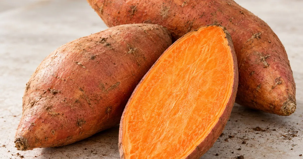 Fresh sweet potatoes with one cut open showing orange flesh