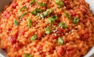Bowl of creamy tomato rice topped with sliced green onions and sesame seeds.